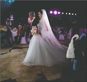  ??  ?? Bride Chen Yaxuan walks down the aisle with her father during an unmasked wedding banquet in Beijing.