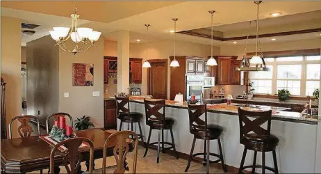  ??  ?? Separating the dining area and kitchen, a long granite breakfast bar is accented by contempora­ry hanging lights.