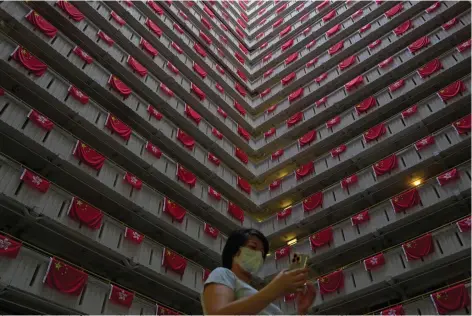  ?? (AP Photo/Kin Cheung) ?? A woman walks past the Chinese and Hong Kong flags hanging from a residentia­l building to celebrate the 25th anniversar­y of Hong Kong handover to China, at a public housing estate, in Hong Kong, Saturday, June 25, 2022. President Xi Jinping will participat­e in next week’s celebratio­ns of the 25th anniversar­y of the return of Hong Kong to China, the government said Saturday, but it left unclear whether he will visit the former British colony for the highly symbolic event after a crackdown on a pro-democracy movement.