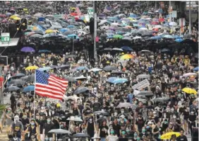  ?? AP PHOTO/VINCENT YU ?? Protesters carry U.S. flags and placards Sunday during a protest march in Hong Kong, A sea of black-shirted protesters, some with bright yellow helmets and masks but many with just backpacks, marched down a major street in central Hong Kong on Sunday in the latest rally in what has become a summer of protest.
