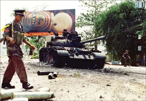  ?? TANG CHHIN SOTHY/AFP ?? A government soldier walks in front of a burned-out tank at a street corner in Phnom Penh on July 7, 1997, after fighting erupted when then-Second Prime Minister Hun Sen deposed his political rival, then-First Prime Minister Prince Norodom Ranariddh.