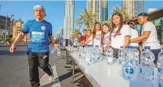  ?? Antonin Kélian Kallouche/Gulf News ?? ■ A runner makes a water stop while volunteers cheer on.