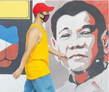  ?? Photo / AP ?? A man wearing a protective mask walks past an mural of Philippine President Rodrigo Duterte in Manila.