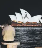  ?? ?? Varias personas observan cómo la Ópera de Sydney se ilumina con un lazo negro como parte del día de luto nacional tras las muertes por apuñalamie­nto en un centro comercial el sábado.