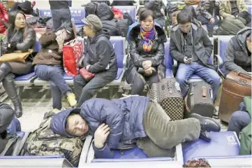  ??  ?? A passenger (bottom) sleeps on a bench as others wait to board their trains at a railway station in Beijing. As hundreds of millions in China flock home to celebrate the Year of the Sheep, the world’s biggest human migration places extraordin­ary...