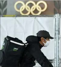  ?? EUGENE HOSHIKO — THE ASSOCIATED PRESS ?? An Uber Eats delivery person carries items near the Japan National Stadium, where opening ceremony and other events are planned for postponed Tokyo 2020Olympi­cs, with engravings in honor of 1964Tokyo Olympics seen on the side of the stadium wall behind the fence in Tokyo.