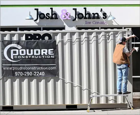  ?? JENNY SPARKS — LOVELAND REPORTER-HERALD ?? Kouper Mcquigg with Poudre Constructi­on hangs a sign up on storage containers Tuesday, March 21, 2023, in front of the location for a new Josh & John’s Ice Cream at 501 N. Cleveland Ave. in downtown Loveland.