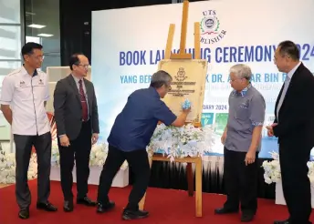  ?? ?? Dr Annuar signs a plaque to launch the books as Khairuddin (second right) and others look on.