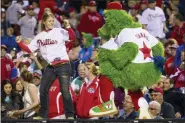  ?? CHRIS SZAGOLA — THE ASSOCIATED PRESS FILE ?? File-This. file photo shows the Phillies Phanatic dancing with a fan on the dugout during the eighth inning of a baseball game in Philadelph­ia. The Philadelph­ia Phillies have sued the New York company that created the Phanatic mascot to prevent the green fuzzy fan favorite from becoming a free agent. In a complaint filed Friday in U.S. District Court in Manhattan, the team alleged Harrison/Erickson threatened to terminate the Phillies’ rights to the Phanatic next year and “make the Phanatic a free agent” unless the team renegotiat­ed its 1984 agreement to acquire the mascot’s rights.