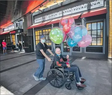  ?? Allen J. Schaben Los Angeles Times ?? DONALD TARBELL, 90, aided by caretaker Ted Forro, celebrates the easing of coronaviru­s restrictio­ns in Orange County with balloons and a shopping trip to reopened South Coast Plaza in Costa Mesa on Thursday.