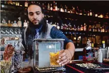  ?? Michael Wyke/Contributo­r ?? Bartender Zarion Clements removes a Smokin’ Gun Old Fashioned from the smoke box at Federal American Grill.