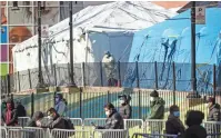  ?? JOHN MINCHILLO/ AP ?? A medical worker looks out onto a line of patients waiting for virus testing Friday outside Elmhurst Hospital Center in
New York.