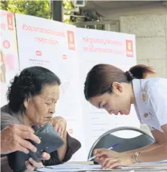  ?? KITJA APICHONROJ­AREK ?? An employee of the Government Savings Bank helps an elderly woman who registered with the bank to receive government welfare for low-income people.