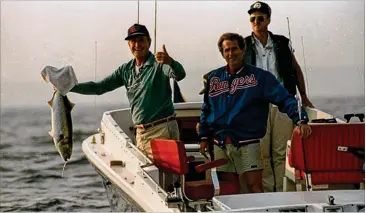  ?? ELISE AMENDOLA / AP ?? President George Bush gives a thumbs up as he holds a 12-15-pound bluefish he caught while fishing near his family’s beloved vacation home in Kennebunkp­ort, Maine, in 1991. At right is his son George W. Bush, in a Texas Rangers jacket, and a Secret Service agent. Bush loved spending summers at the family’s New England retreat.