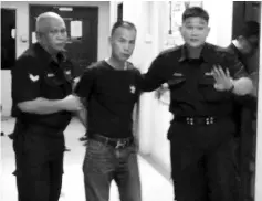  ??  ?? Li being escorted out of the Magistrate’s Court in Tawau yesterday.