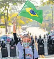  ?? AP ?? ■
A resident of Sao Paulo’s Paraisopol­is slum waves a Brazil flag as police stand by during a protest demanding the state government pay more attention to slums amid Covid-19-related curbs.