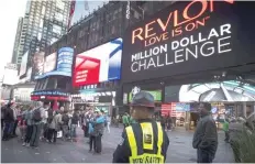  ?? — Reuters ?? A public safety officer keeps watch as people stand in front of a billboard owned by Revlon in Times Square in the Manhattan borough of New York.