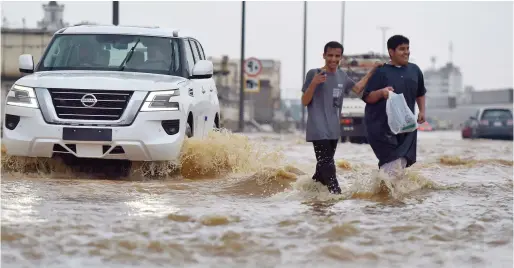  ?? ?? Men walk in a flooded street following heavy rains in the Saudi coastal city of Jeddah on Thursday.