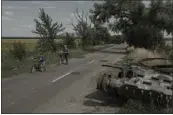  ?? EMILE DUCKE — THE NEW YORK TIMES ?? People bike past the remains of a tank in the Chernihiv region of Ukraine last month.
