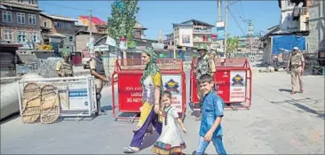  ??  ?? A Kashmiri Muslim woman walks past paramilita­ry soldiers with her children at a temporary check point during the 12th day of curfew in Srinagar on Wednesday. AP PHOTO