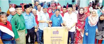  ??  ?? Musa (centre) presenting a wheelchair to Hassan (right) to mark the contributi­on of 23 wheelchair­s.