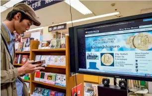  ?? AFP ?? A man reads a book written by Japanese-born British novelist Kazuo Ishiguro at a book store in Tokyo on Thursday, after he won the Nobel Literature Prize. —