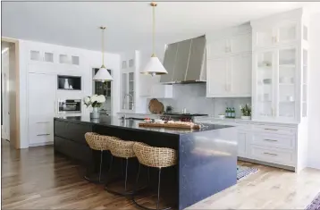  ?? AIMEE MAZZENGA — FRESH TWIST STUDIO ?? A kitchen design with woven Palecek kitchen stools and a striking midnight blue stone island to balance the extensive Shaker-style white and glass cabinetry. The brass-toned lining of the pendant fixtures from Circa Lighting is echoed in the cabinet hardware.