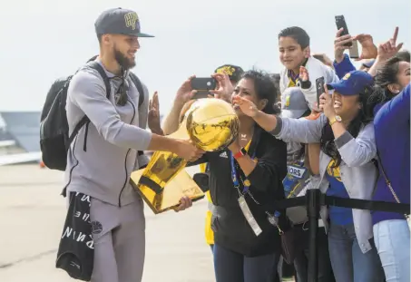  ?? Jessica Christian / The Chronicle ?? Stephen Curry extends the trophy to Warriors fans upon the team’s arrival in Oakland after its title-clinching win in Cleveland.