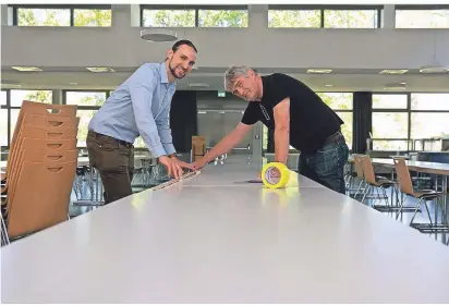  ?? NGZ-FOTO: TINTER ?? Start-vorbereitu­ngen in der Mensa der Gesamtschu­le Nordstadt: Jonas und Ralf Franke (v.l.) kleben Abstands-markierung­en auf die Tische.