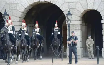  ?? — AFP ?? An armed police officer (2R) and a military personnel (R) stand guard as the Household Cavalry leave the Horse Guards Parade in central London on Saturday.