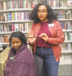  ??  ?? Candice Washington, circulatio­n assistant at P.D. Brown Memorial Library, demonstrat­es protective hairstyles on DauVeen Walker, reference supervisor at the library.