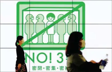  ?? AFP ?? People wearing face masks walk past a public service display promoting social distancing at a concourse leading to the terminal station in Tokyo’s Shinjuku district on April 18.