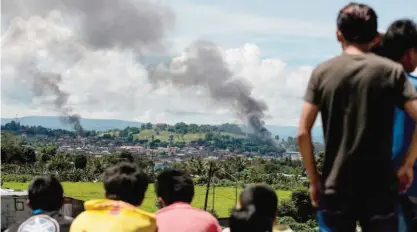  ??  ?? MARAWI, Philippine­s: People watch as smoke billows from houses after aerial bombings by Philippine air force planes on militant positions yesterday. — AFP