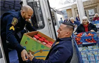 ?? BILL LACKEY / STAFF ?? Springfiel­d Police Officer Zach Massie hands off a box of peanut butter to Sgt. Deric Nichols as they load a vehicle with Thanksgivi­ng dinners and other food for Operation Thanksgivi­ng at the Springfiel­d Meijer on Tuesday. The program has been serving local families in need for 30 years.