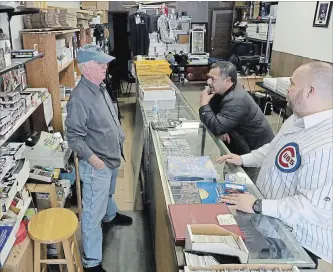  ?? ANTONIO PEREZ CHICAGO TRIBUNE ?? John Merkel. owner of Elite Sports Cards and Comics in Chicago, talks sports with customers Ronnie Holloway and Jose Camacho.