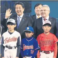  ??  ?? IOC president Thomas Bach, right, and Japanese Prime Minister Shinzo Abe, left, pose with children during a visit to a baseball stadium in Fukushima.