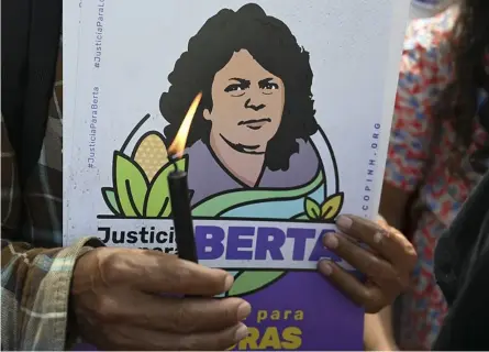  ?? AFP ?? Un miembro del Copinh sostuvo ayer una vela mientras esperaba la lectura de la sentencia sobre el asesinato de la líder ambientali­sta e indígena hondureña Berta Cáceres (en el cartel).