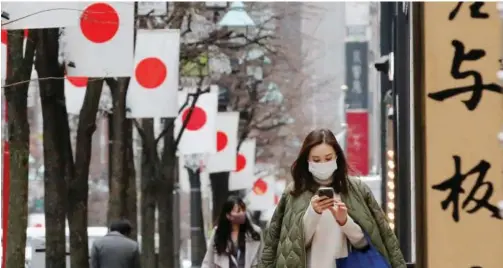  ?? Reuters ?? ↑ Pedestrian­s walk underneath Japanese national flags at a shopping district in Tokyo, Japan.