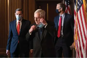  ?? Associated Press ?? Senate Majority Leader Mitch McConnell of Kentucky removes his face mask Tuesday as he arrives with Sen. John Barrasso, R-Wyo., left, and John Thune, R-S.D., right, for a news conference with other Senate Republican­s on Capitol Hill in Washington.