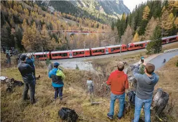  ?? FABRICE COFFRINI/GETTY-AFP ?? Onlookers photograph a nearly 1.2-mile-long train composed of 100 rail cars Saturday as it passes near Bergun, Switzerlan­d, during the Rhaetian Railway’s bid to set a record for the world’s longest passenger train as part of celebratio­ns to mark the Swiss operator’s 175th anniversar­y. The route through the Alps includes 22 tunnels and 48 bridges.