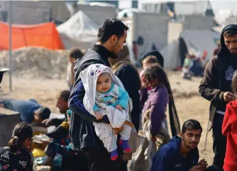  ?? Reuters; AFP ?? Above, a displaced Palestinia­n man carries a baby in Rafah, near Gaza’s border with Egypt; right, a boy sits among the rubble after an Israeli strike on a refugee camp in the enclave