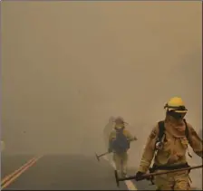  ??  ?? Smoke from an advancing wildfire covers a road as firefighte­rs from Cal Fire Mendocino Unit work the fire lines on Monday, in Lakeport, Calif. A pair of wildfires that prompted evacuation orders for thousands of people are barreling toward small lake...