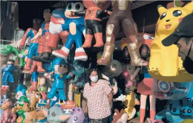  ?? LUIS ANTONIO ROJAS/THE NEW YORK TIMES ?? Maricela Ortega stands among an array of piñatas last month at her husband’s shop in Mexico City. The piñata industry, dependent on social gatherings, has seen sales plummet because of the coronaviru­s pandemic.