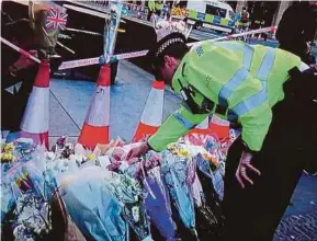  ??  ?? A police officer placing flowers in Westminste­r, London, yesterday.