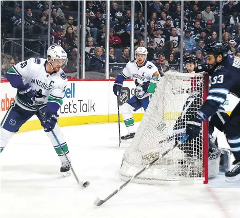  ?? PHOTO BY JONATHAN KOZUB/NHLI VIA GETTY IMAGES ?? Vancouver Canucks captain Henrik Sedin carries the puck behind the net under pressure from Winnipeg Jets defenceman Dustin Byfuglien during the first period on Sunday in Winnipeg. The Canucks saw little of the Jets’ net in a 1-0 loss.