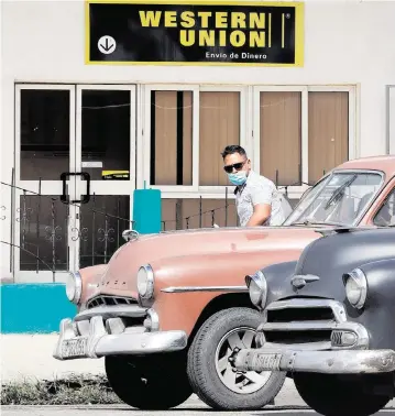  ?? ERNESTO MASTRASCUS­A EFE/Sipa USA | Nov. 23 2020 ?? Two classic cars pass in front of a Western Union office in Havana. Western Union remittance services to Cuba, used by many Miamians to send money to relatives on the island, have been halted since Jan. 28.