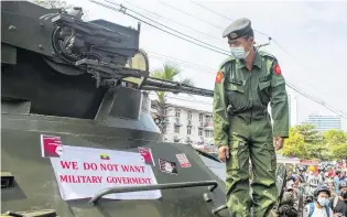  ?? PHOTO: REUTERS ?? Message from the people . . . A soldier looks at a banner attached to a military vehicle outside Myanmar’s Central Bank during a protest against the military coup, in Yangon, yesterday.