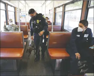  ??  ?? San Diego Metropolit­an Transit System officer Francisco Bautista wears a Fitbit device as he scans a trolley car with his dog July 9 in San Diego. The device is part of a Scripps Research “DETECT” study to monitor a person’s heart rate and allow participan­ts to record symptoms such fever or coughing to share with scientists, in an attempt to see if they can spot covid-19.
(AP/Gregory Bull)