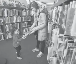  ?? CLOE POISSON/SPECIAL TO THE COURANT ?? In this January 2020 photo, Carissa Fioritto hands some books to her daughter, Heather, 3, during a visit to the Mary Cheney Library in Manchester. The library’s lending of children’s materials was the highest of all public libraries in the state for 2018-19, according to statistics gathered by the Connecticu­t State Library.