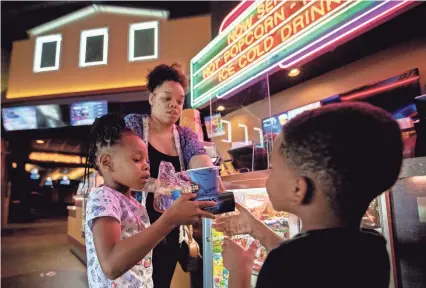  ?? PHOTOS BY MAX GERSH/THE COMMERCIAL APPEAL ?? Charmaine Jacobs hands snacks to her daughter, Skye Jacobs, 6, and son Zaylen Jones, 4, on Monday before seeing “Trolls World Tour” at the Desoto Cinema Grill in Southaven.